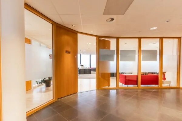 Moderne kantoorruimte aan de 1e Hogeweg met glazen wanden, houten deuren en een wachtruimte met rode banken.